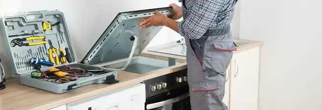 Cooktop repair technician lifting a built-in stovetop for service in Anchorage, AK