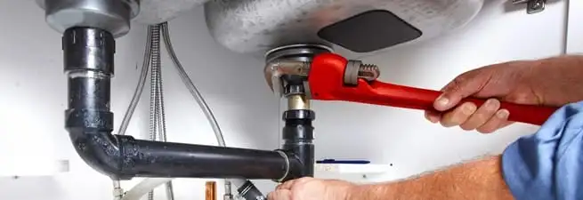 Garbage disposal repair technician tightening the sink drain and disposal connection in Anchorage, AK