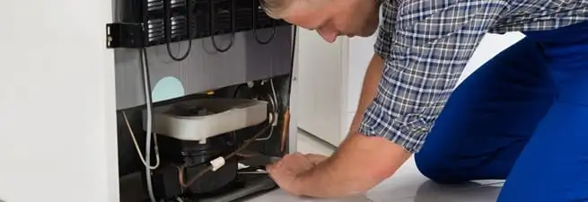 Refrigerator repair technician servicing the compressor and condenser area in Anchorage, AK