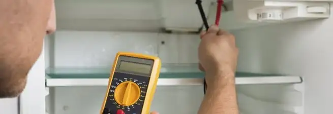 Refrigerator repair technician testing electrical components with a multimeter in Anchorage, AK